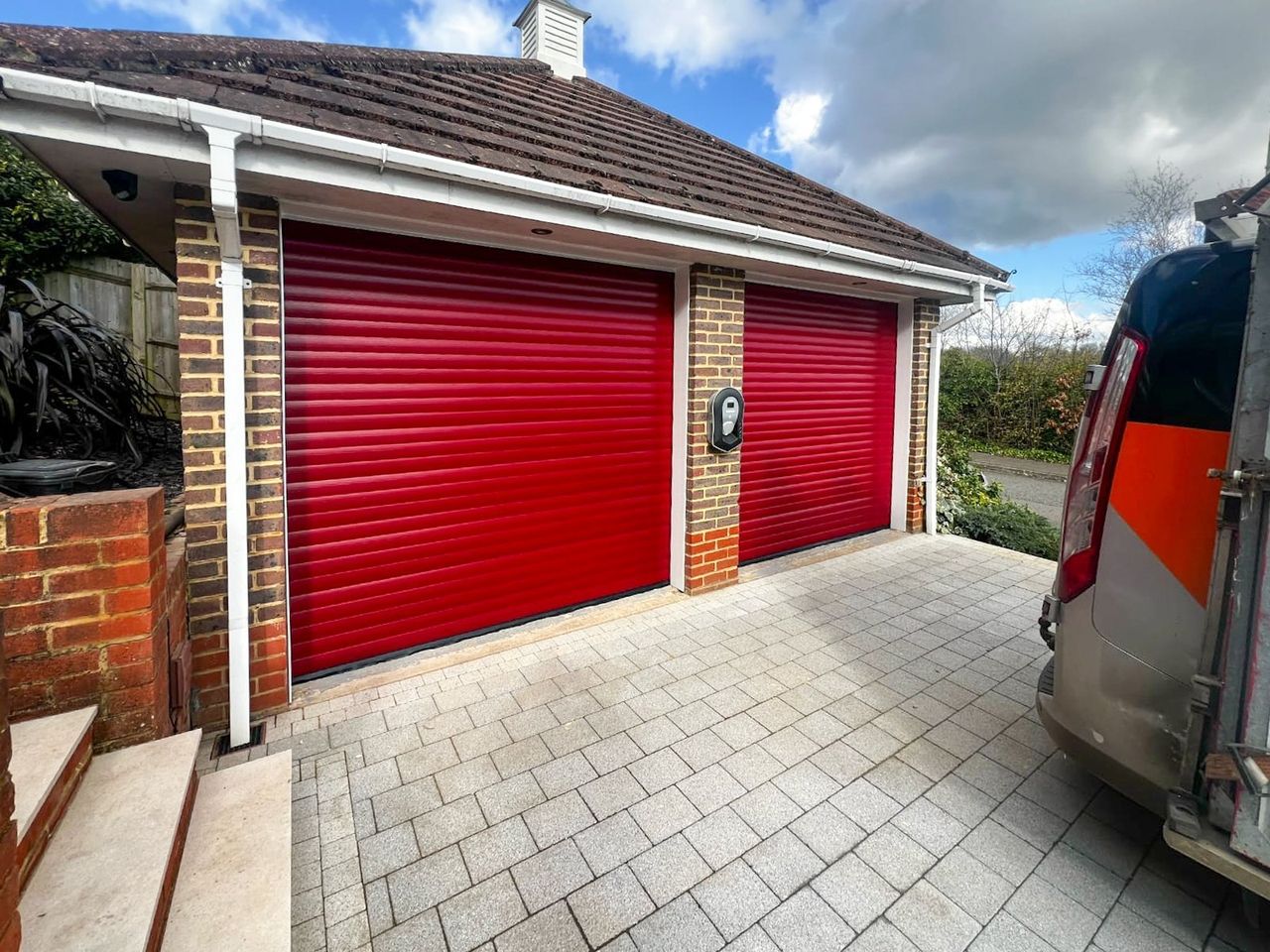Red insulated aluminium roller garage door fitted to a brick detached garage