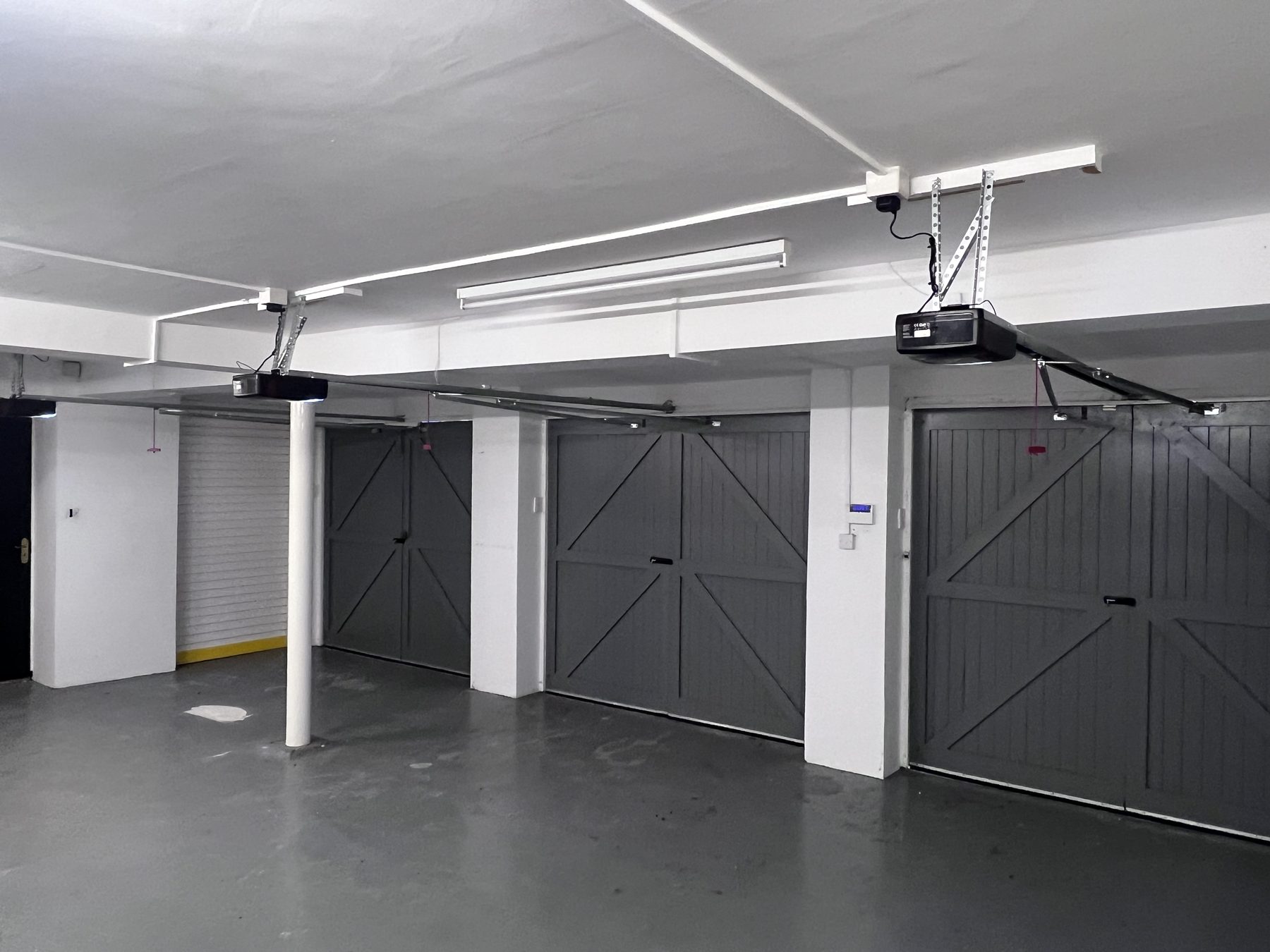 Three bays of motorised side-hinged garage doors fitted by Wolverine, each with a ceiling-mounted operator and arm gear