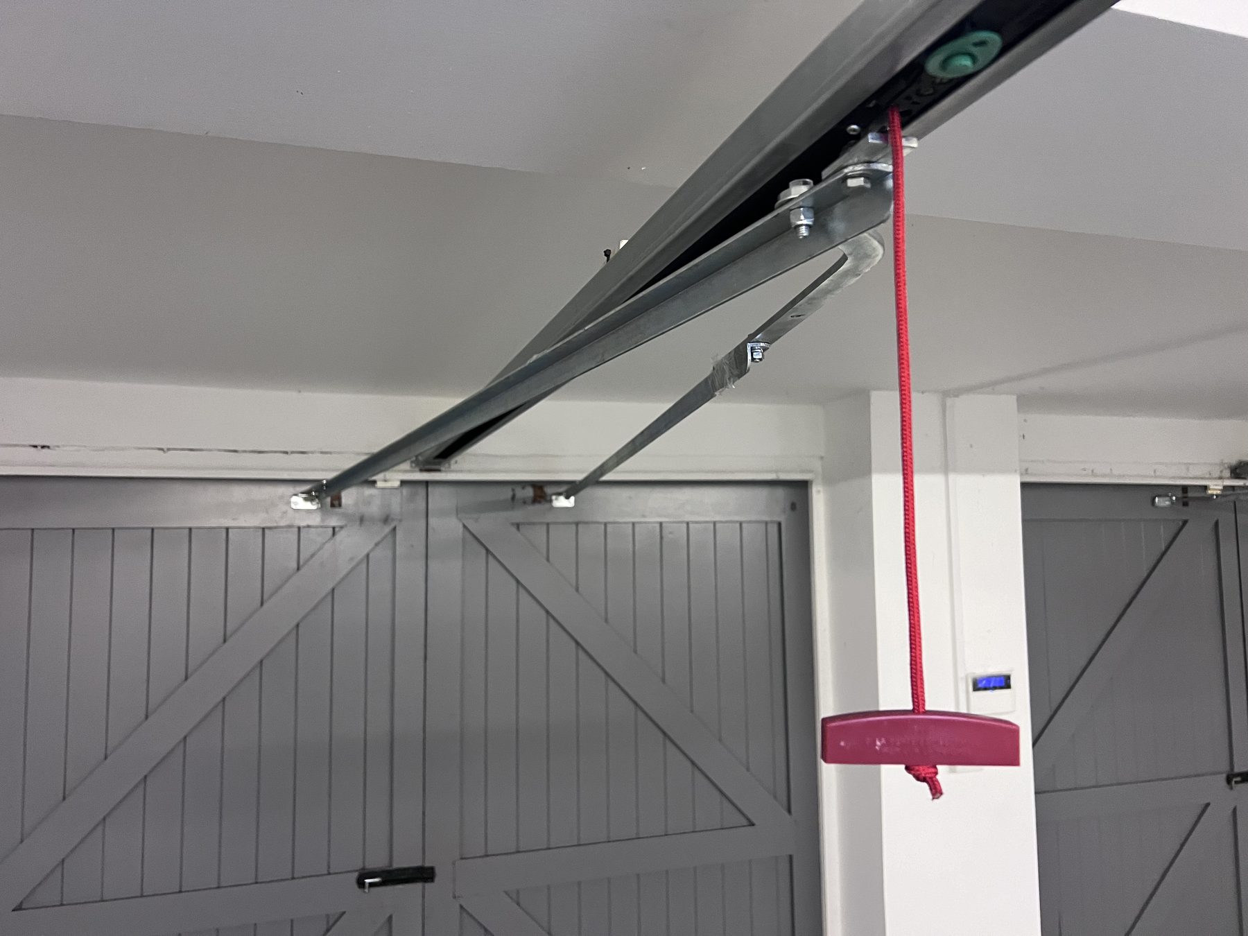 Close-up of the operator arm and red manual release cord on a motorised side-hinged garage door